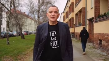 Jan van Aken in einem Wohnviertel. Sakko über ein T-Shirt mit der Aufschrift "tax the rich" - besteuert die Reichen.